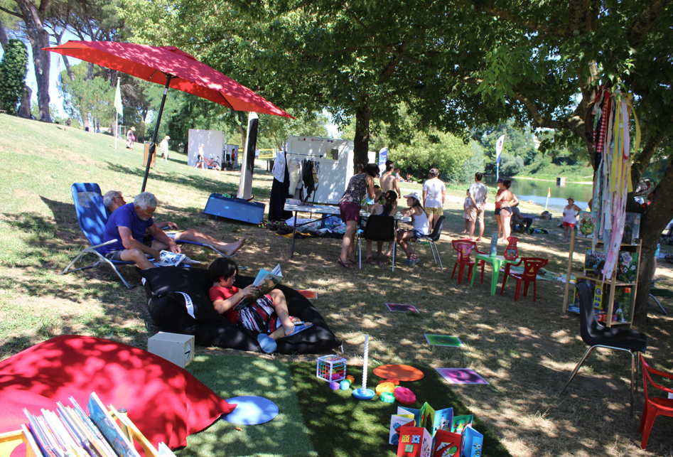 Photo des installations mises en place l'été on y voit des jeux pour les enfants, des livres, des poufs, des personnes en train de lire à l'ombre des arbres sur des transats ou poufs