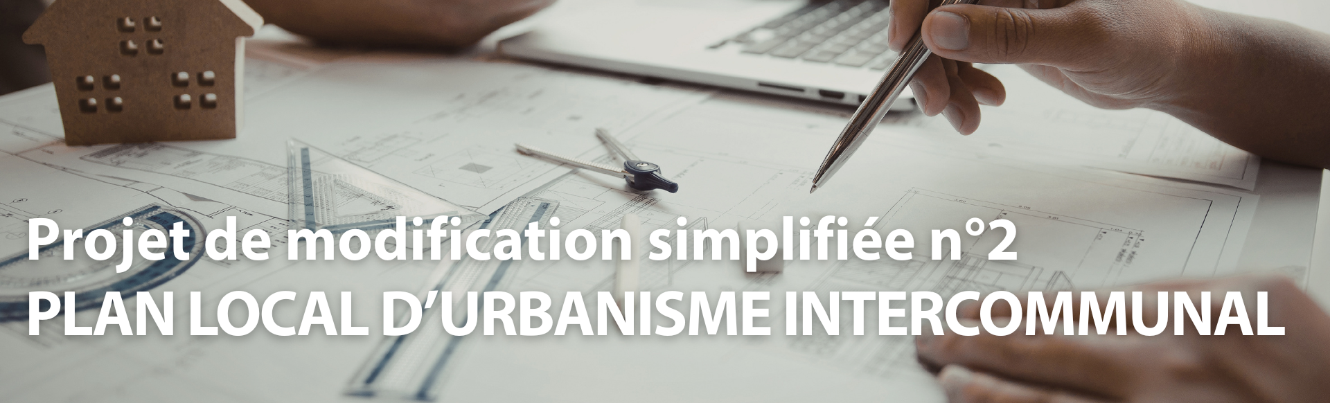 mains avec stylo, et table avec plan architecte et instruments pour dessiner (compas, équerre, règle, etc.)