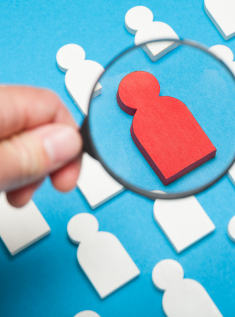 Une loupe qui montre une silhouette rouge au milieu de silhouettes blanches